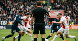 Referee standing on soccer field with players competing for the ball